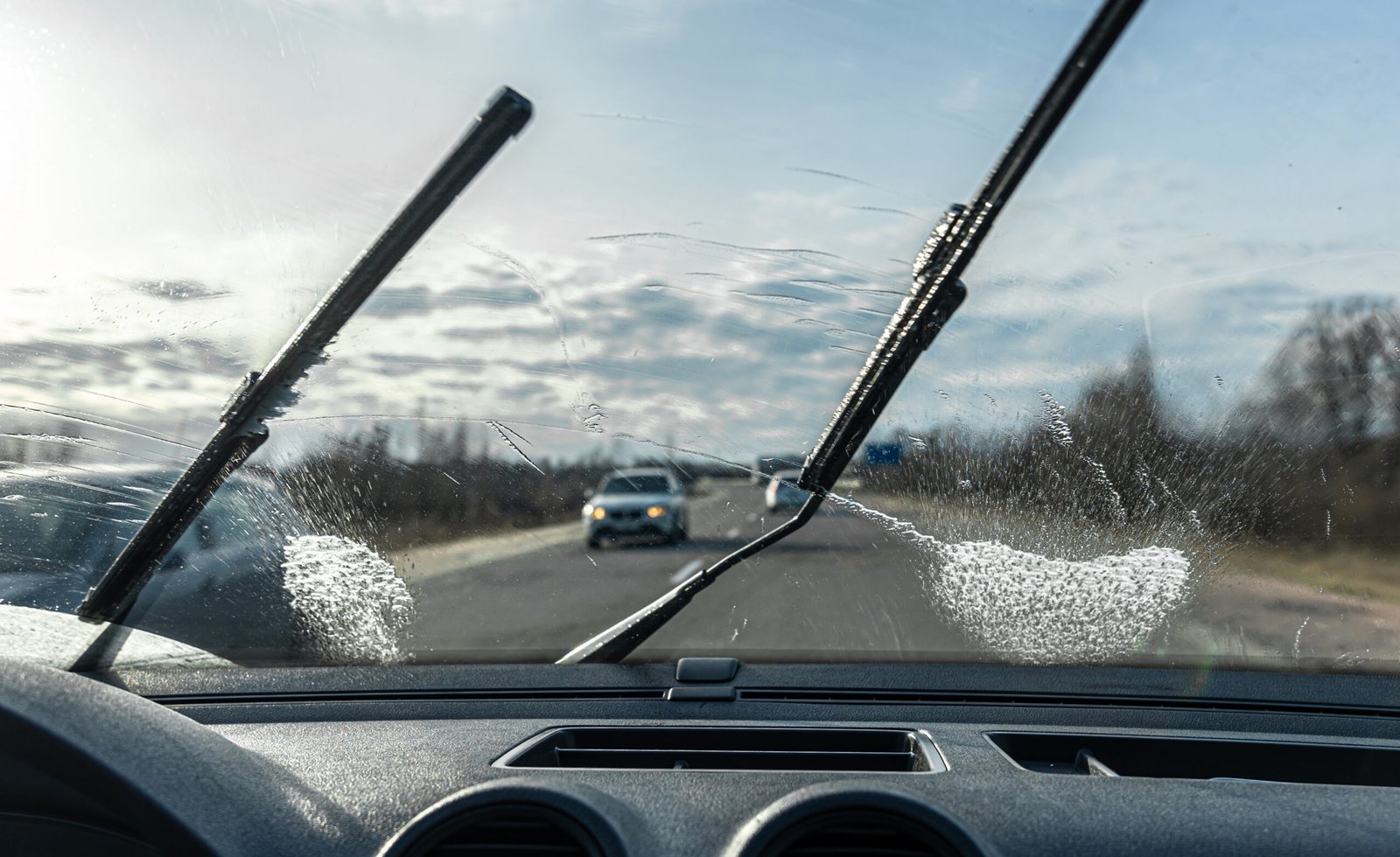 Car wipers clean windshields when driving in sunny weather, inside view.